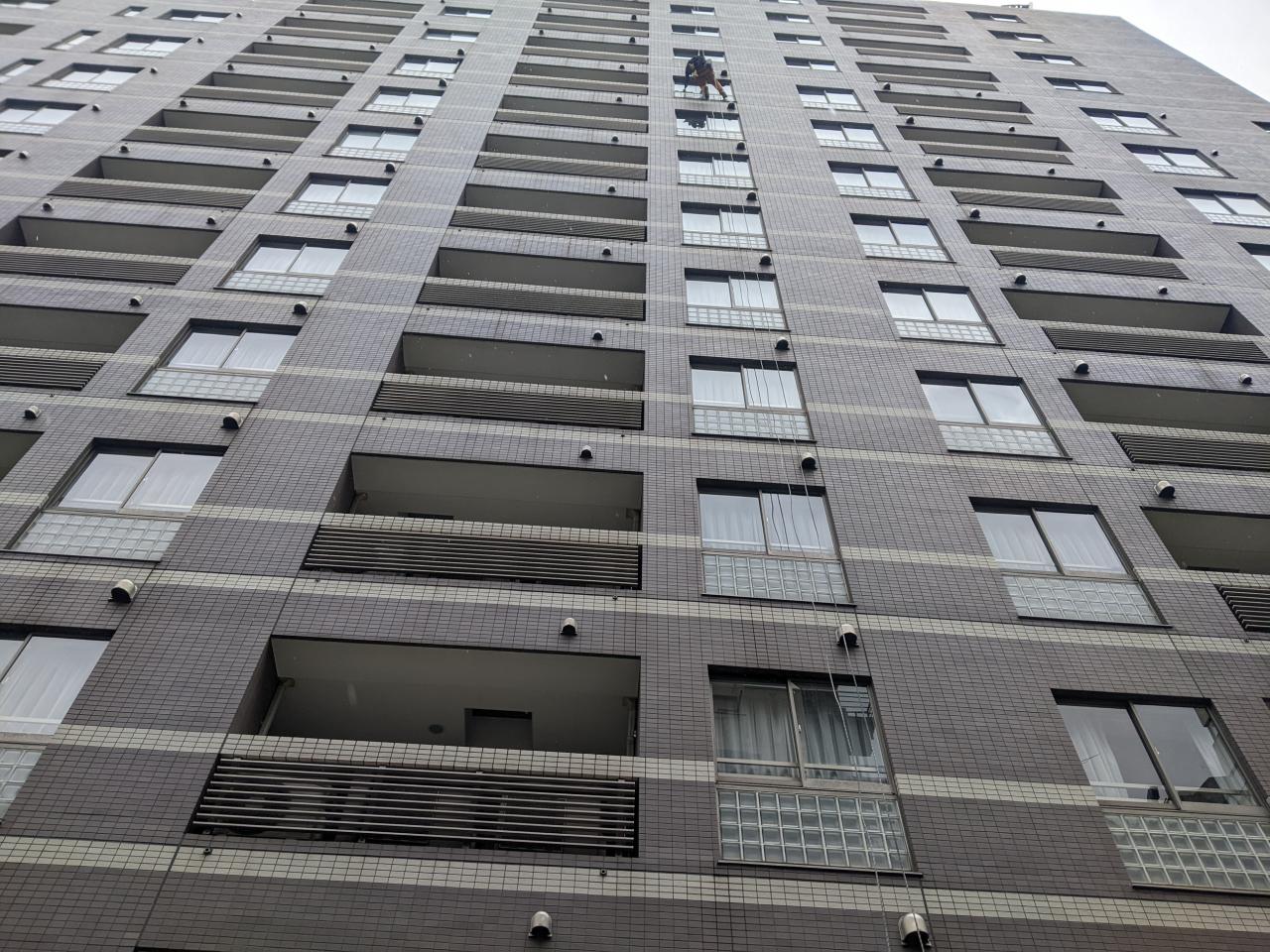 高層マンションのタイル外壁でロープ高所作業により清掃を行う作業員